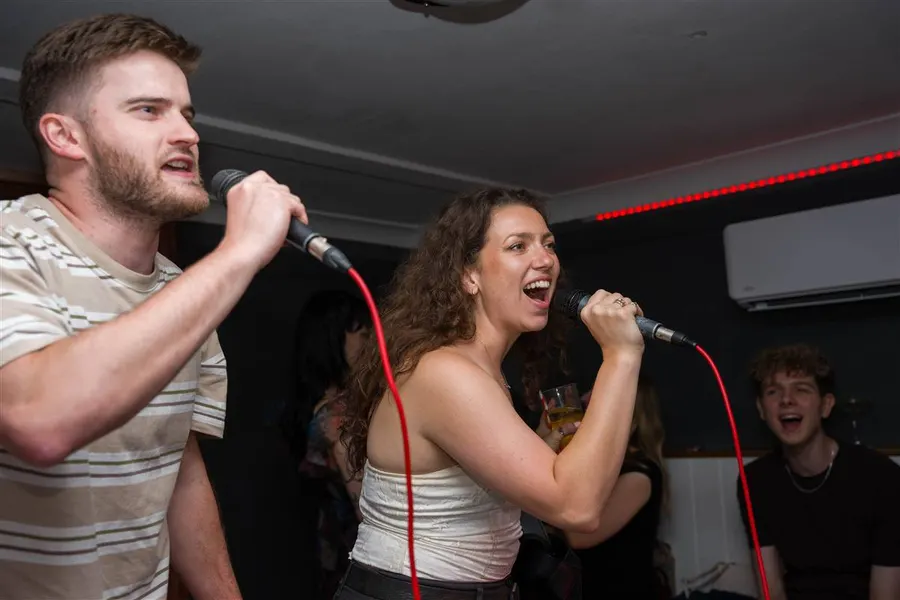 Two people belting a duet under the red LED of a karaoke room